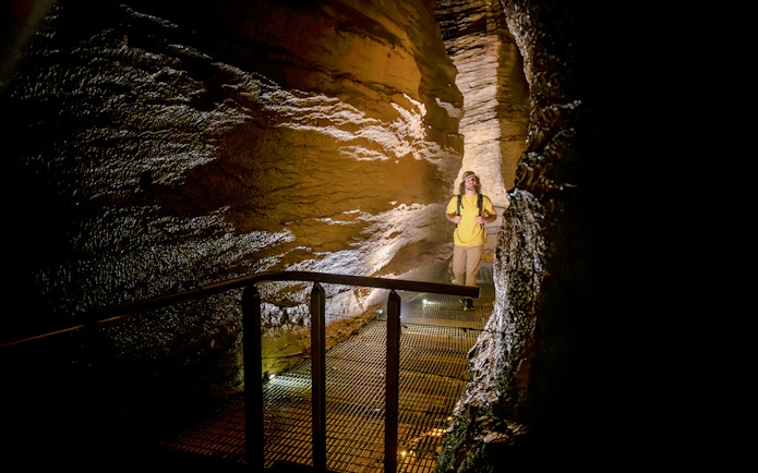 Tourist walking through illuminated Te Anau Glowworm Caves on guided tour.