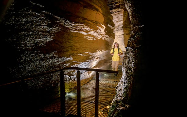 Tourist walking through illuminated Te Anau Glowworm Caves on guided tour.