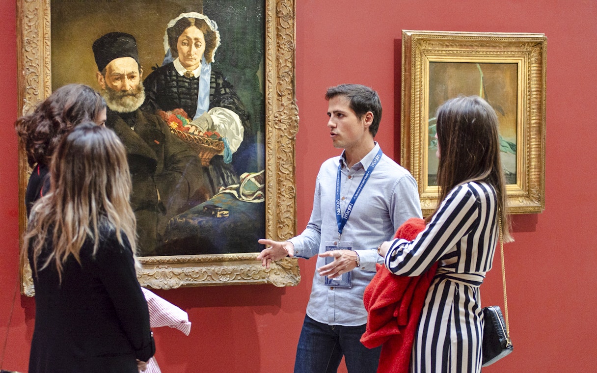 Guide explaining paintings to tourists inside Orsay Museum, France.