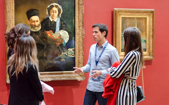 Guide explaining paintings to tourists inside Orsay Museum, France.