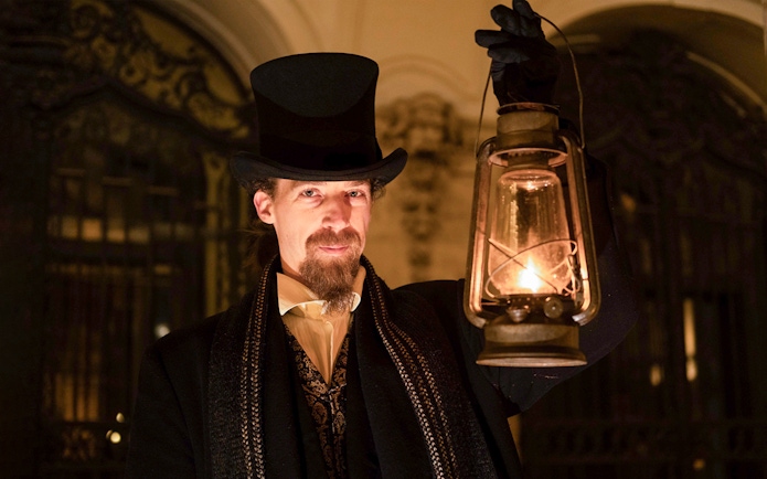Guide in period costume holding lantern during Budapest Buda Castle evening tour.