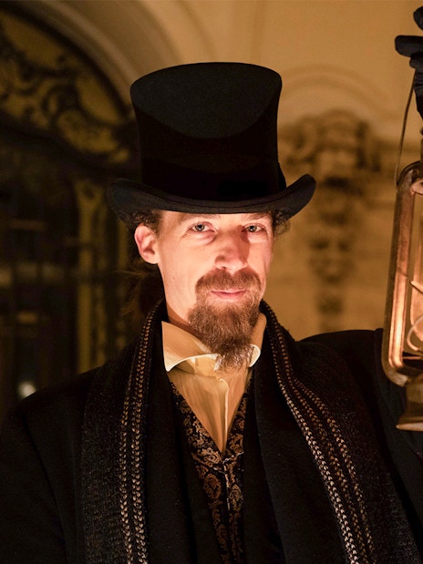 Guide in period costume holding lantern during Budapest Buda Castle evening tour.