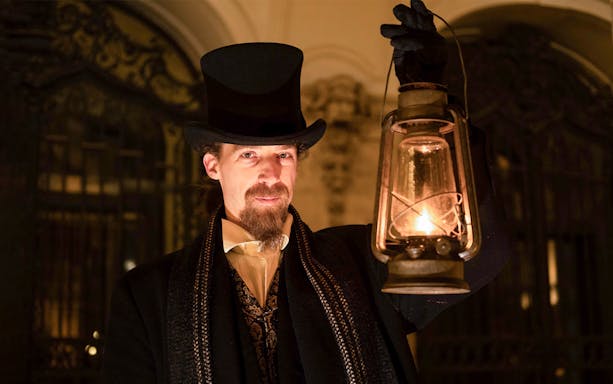 Guide in period costume holding lantern during Budapest Buda Castle evening tour.