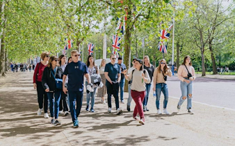 Tour group walking along a tree-lined path with Union Jack flags, part of the Changing of the Guard Experience.