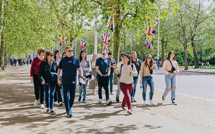 Tour group walking along a tree-lined path with Union Jack flags, part of the Changing of the Guard Experience.