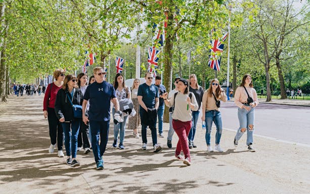 Tour group walking along a tree-lined path with Union Jack flags, part of the Changing of the Guard Experience.