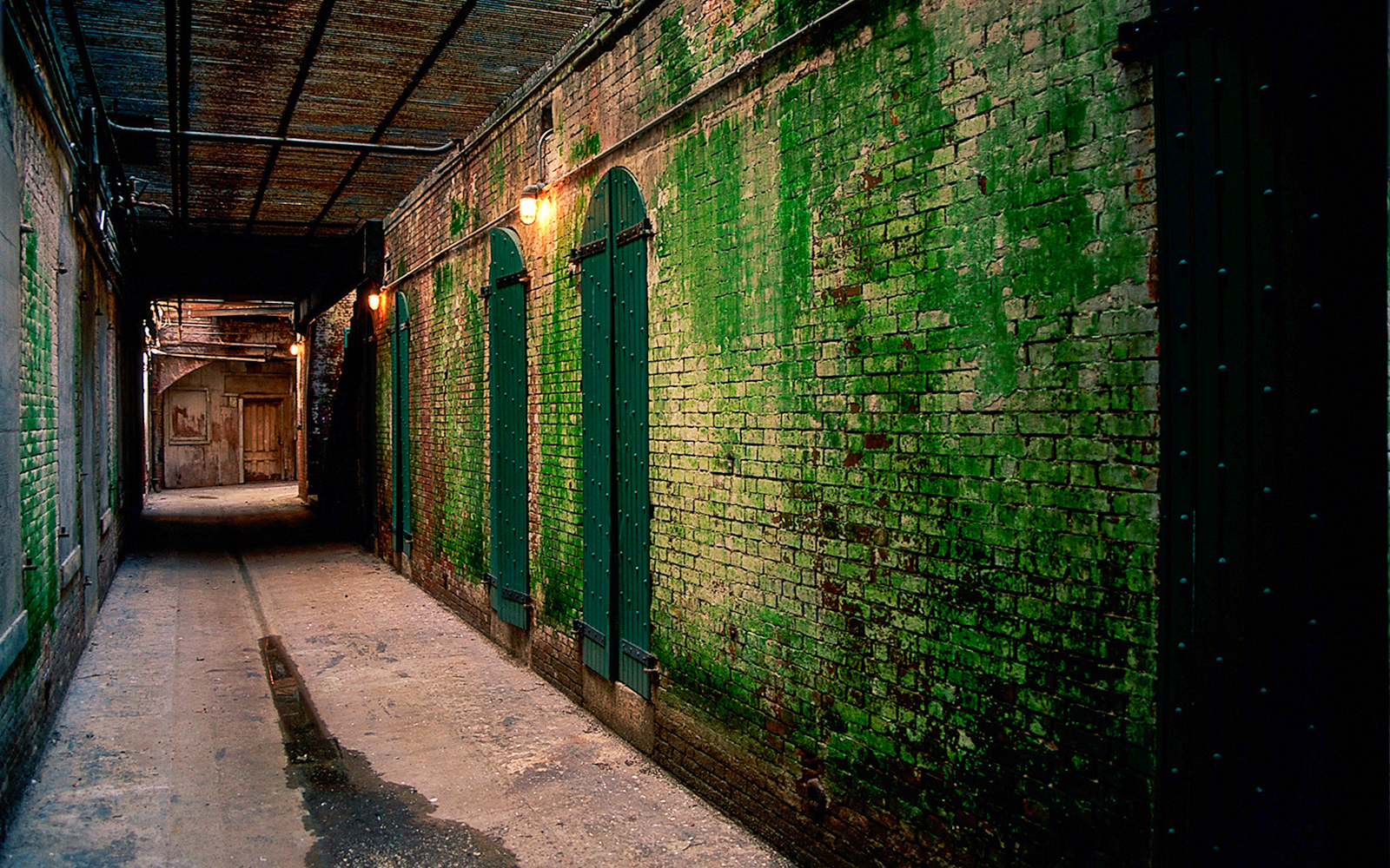 Dimly lit Alcatraz corridor with green brick walls at night.