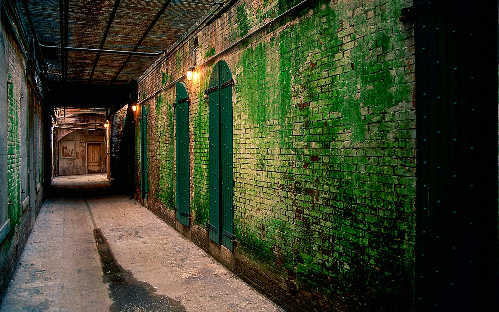 Dimly lit Alcatraz corridor with green brick walls at night.