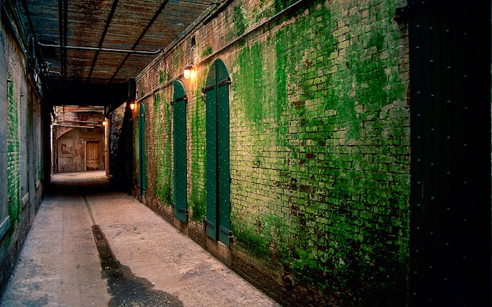 Dimly lit Alcatraz corridor with green brick walls at night.