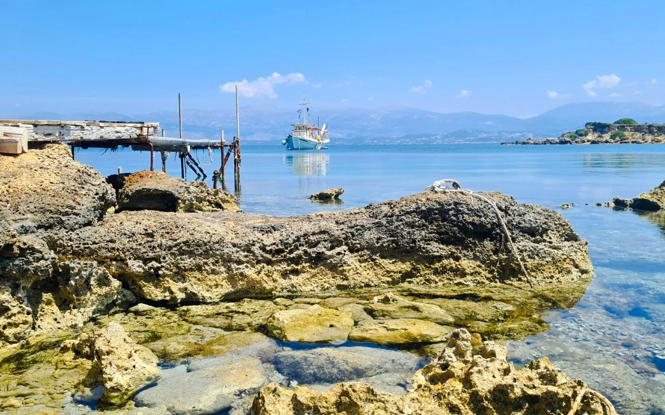 Boat near rocky shore with wooden pier, Kefalonia daily cruise.
