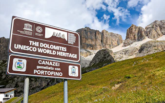 Sign for Dolomites UNESCO World Heritage site with mountains in background, Canazei, Italy.
