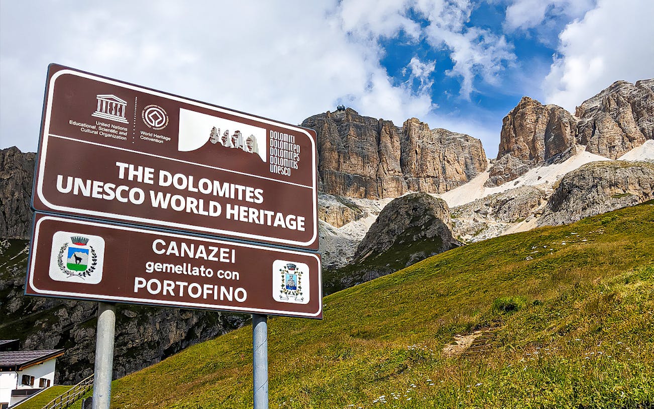 Sign for Dolomites UNESCO World Heritage site with mountains in background, Canazei, Italy.