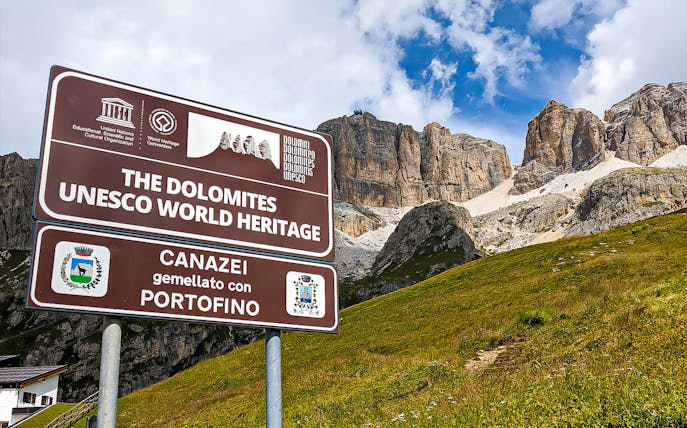 Sign for Dolomites UNESCO World Heritage site with mountains in background, Canazei, Italy.