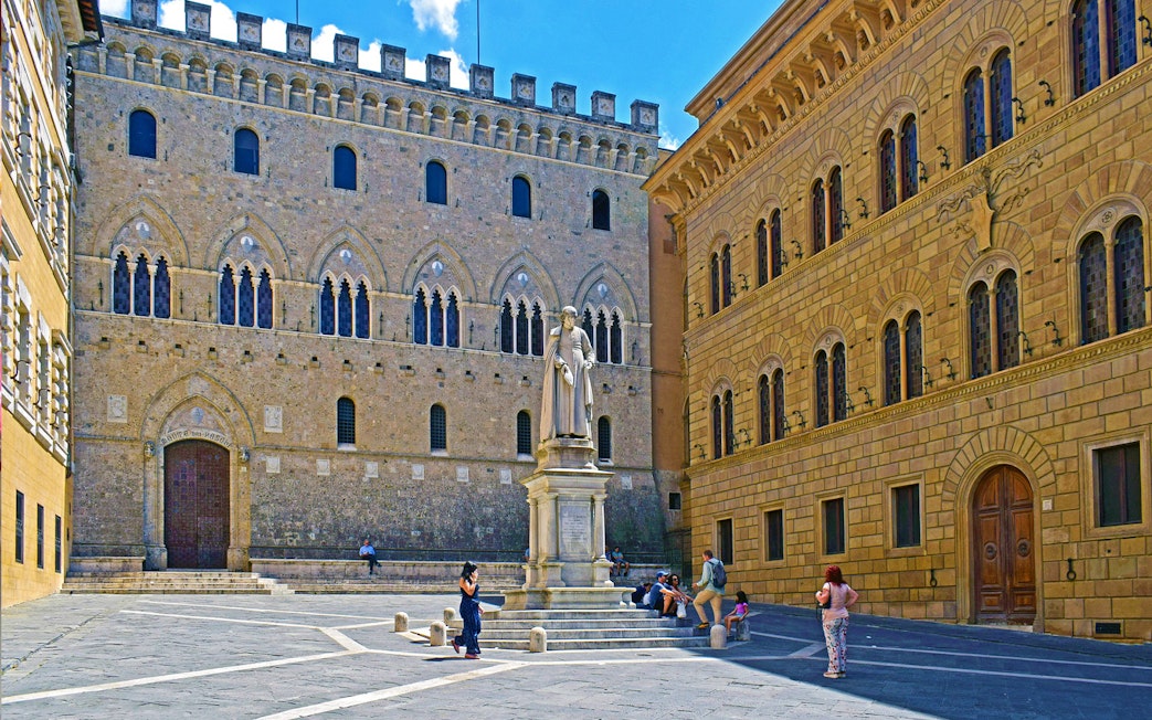 Siena's Piazza Salimbeni with historic buildings and statue, part of small-group guided tour.