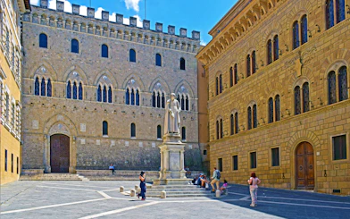 Siena's Piazza Salimbeni with historic buildings and statue, part of small-group guided tour.