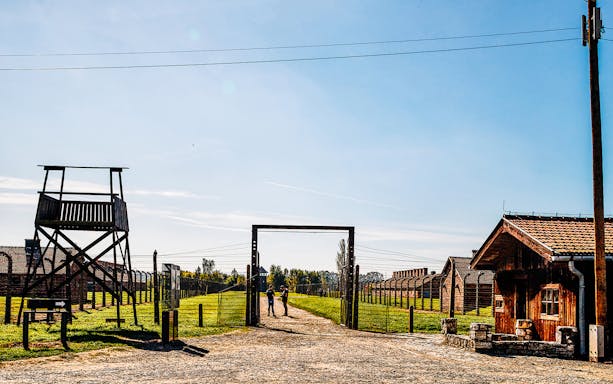 Auschwitz-Birkenau entrance with watchtower and barracks under a clear sky.
