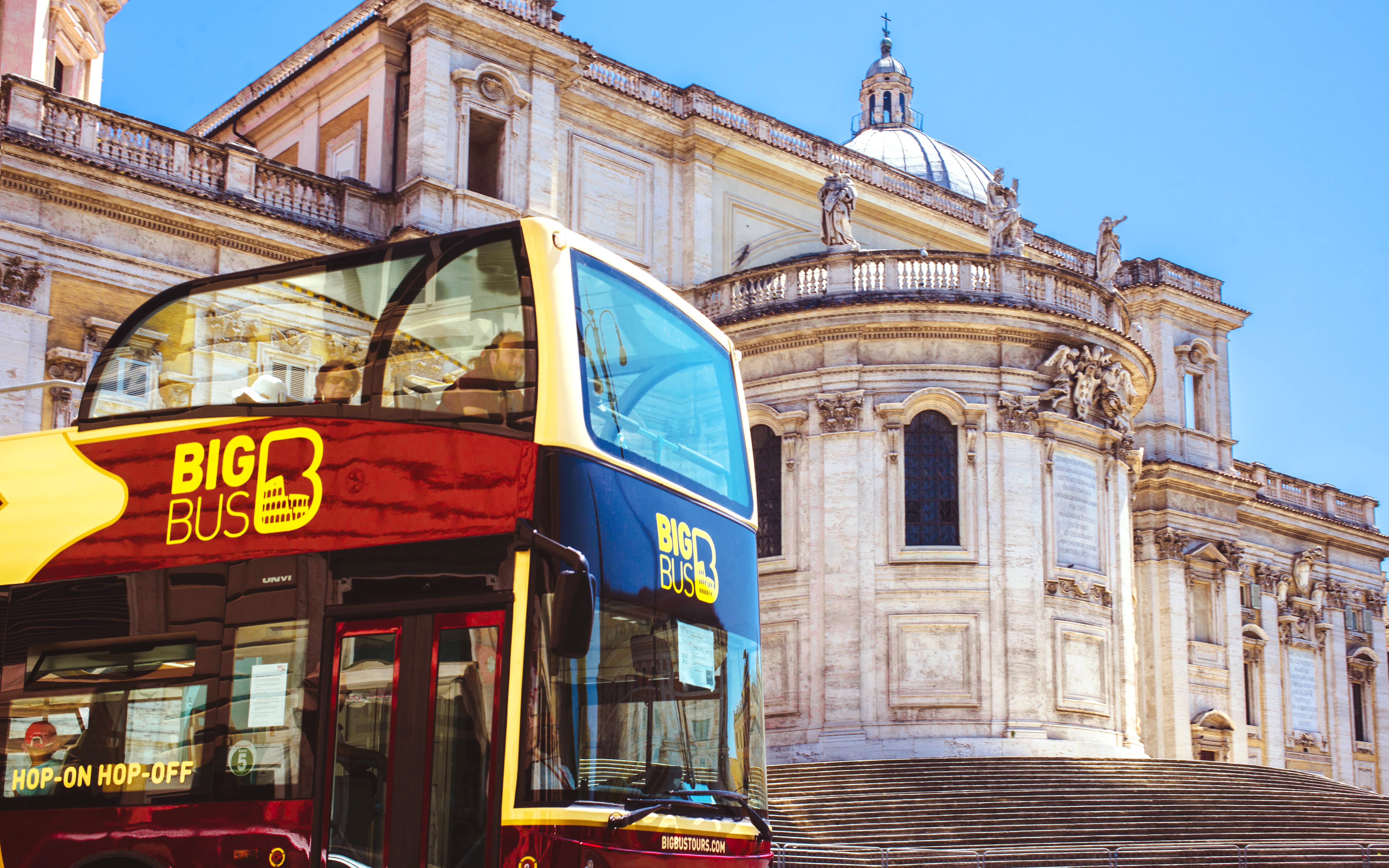 Hop-on hop-off bus in front of historic building in Rome.