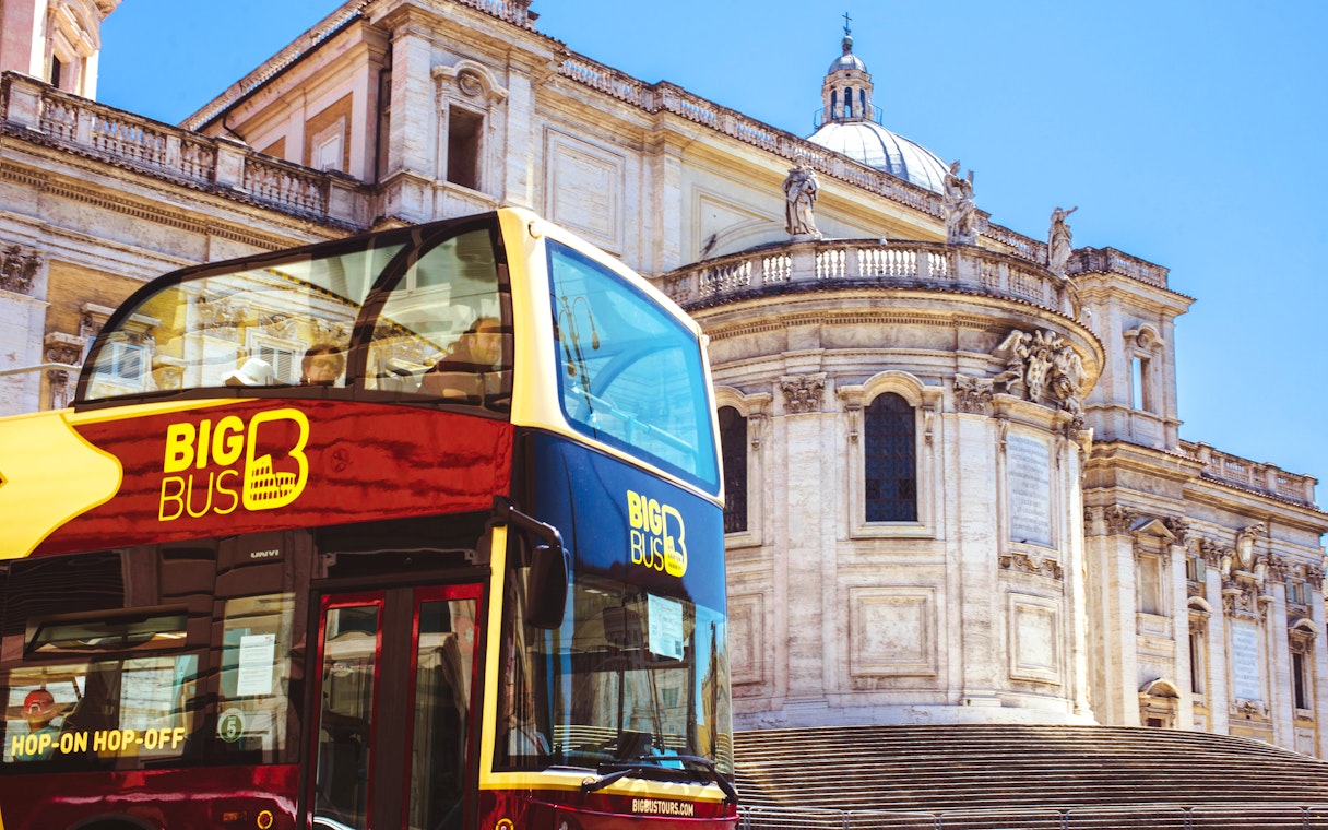Hop-on hop-off bus in front of historic building in Rome.