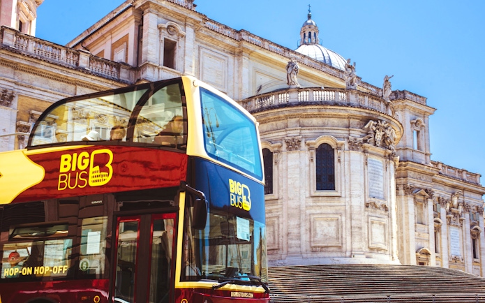 Hop-on hop-off bus in front of historic building in Rome.