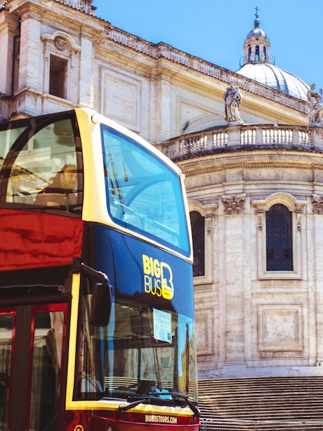 Hop-on hop-off bus in front of historic building in Rome.