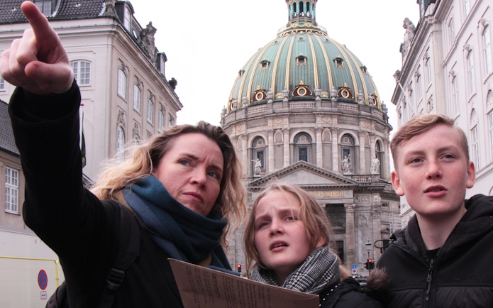 Mystery hunt participants at Amalienborg Palace, Copenhagen, pointing towards a landmark.