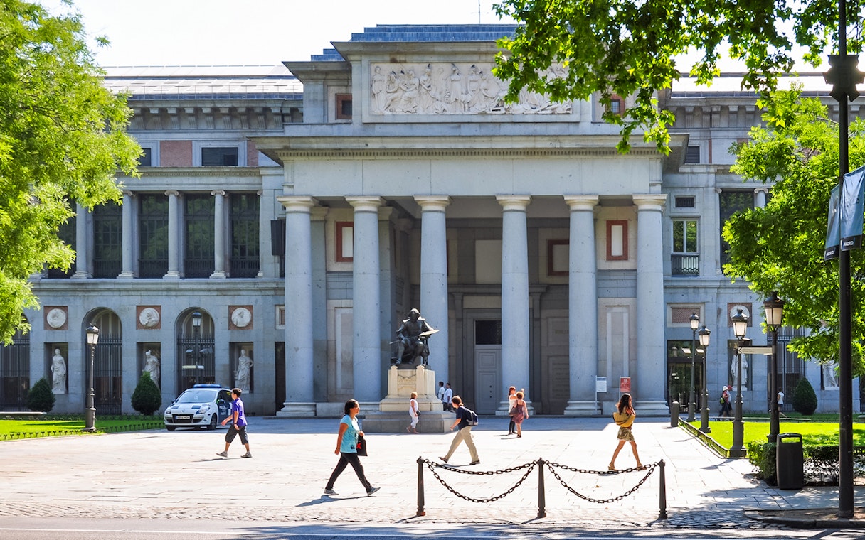 Prado Museum entrance in Madrid with visitors walking nearby.