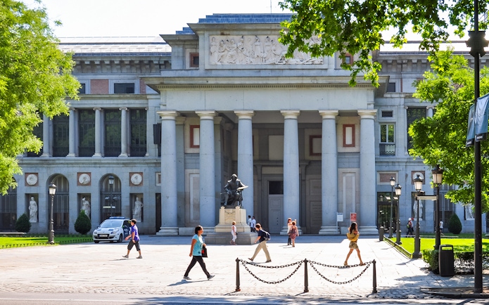 Prado Museum entrance in Madrid with visitors walking nearby.