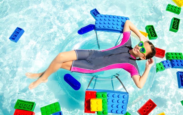 Child relaxing on a float surrounded by large Lego bricks at Legoland Malaysia water park.