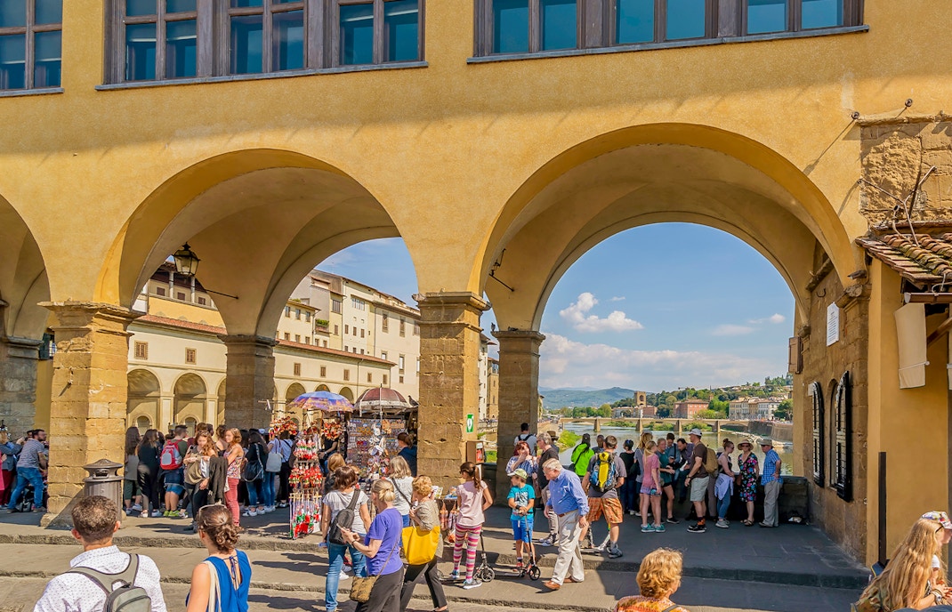 Tourists exploring shops on Ponte Vecchio near Vasari Corridor, Florence.