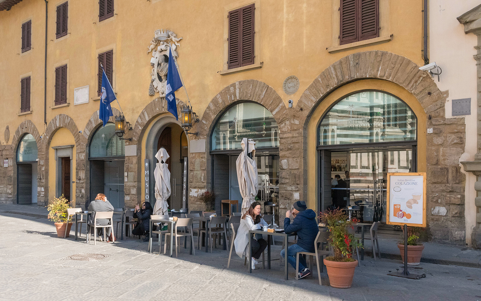 Facade of Opera del Duomo Museum with outdoor seating and visitors in Florence, Italy.