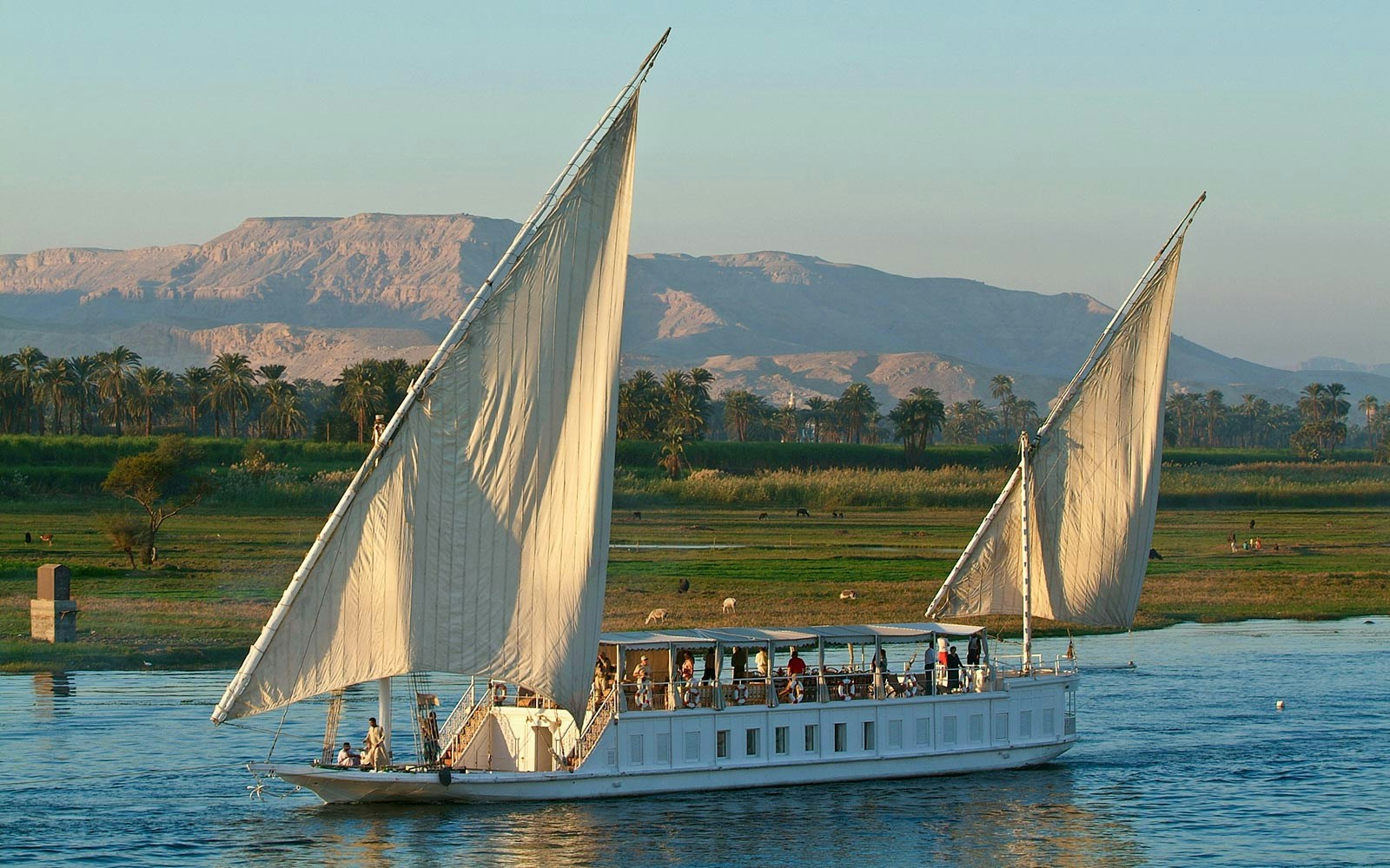 Nile River cruise boat with tourists enjoying views of the river and surrounding landscape in Egypt.