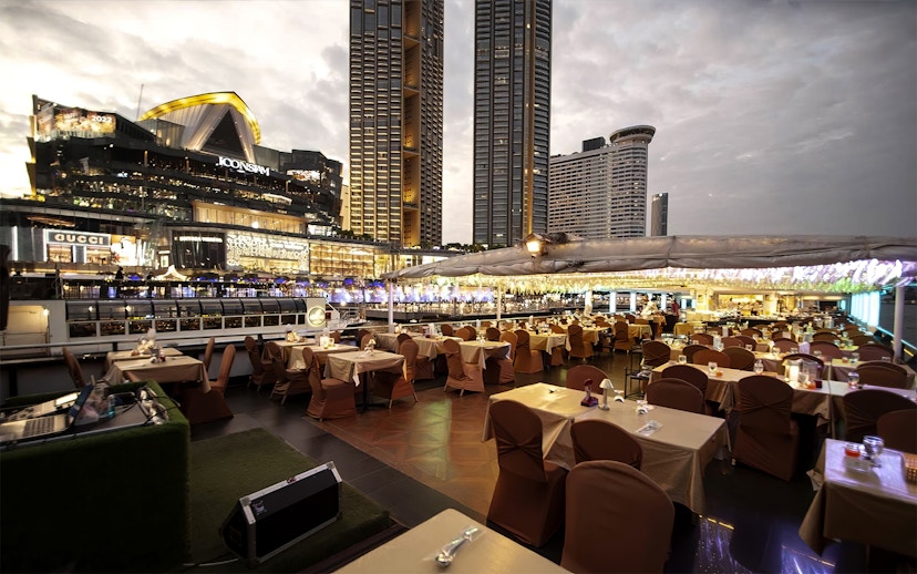 Dinner tables set on Chao Phraya Princess Cruise with Bangkok skyline in view.