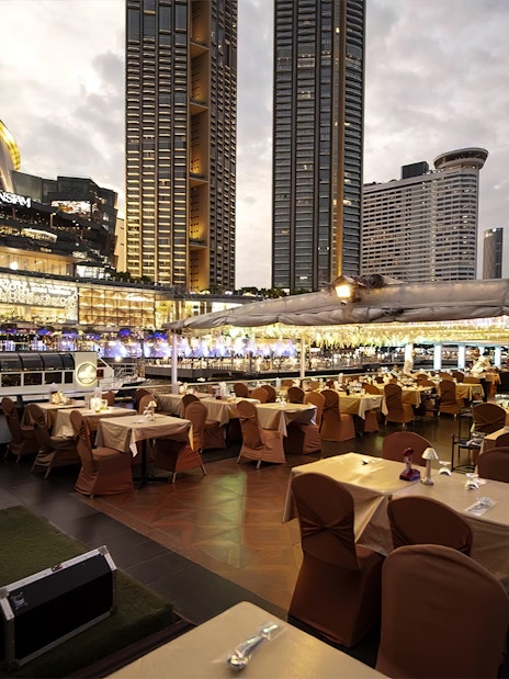 Dinner tables set on Chao Phraya Princess Cruise with Bangkok skyline in view.