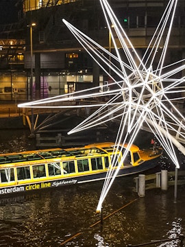 Amsterdam canal boat passing illuminated star sculpture during Light Festival cruise.