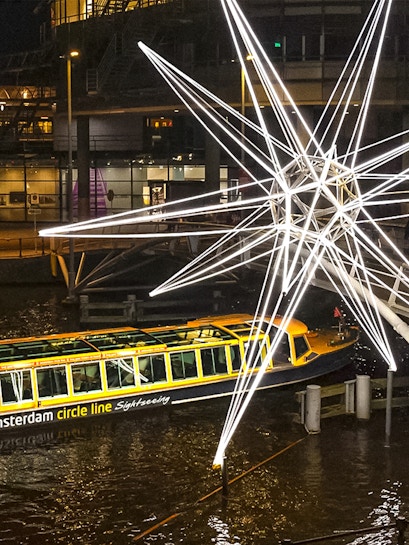 Amsterdam canal boat passing illuminated star sculpture during Light Festival cruise.