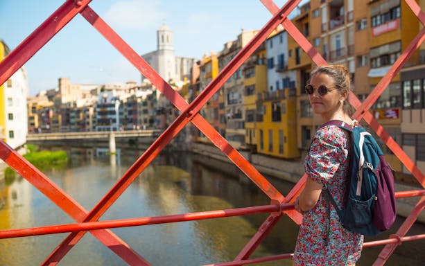 Female traveler on Eiffel Bridge in Girona, overlooking colorful riverside buildings.