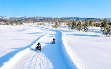 Snowmobiling on a snowy trail with trees and mountains in Bibai, Hokkaido.