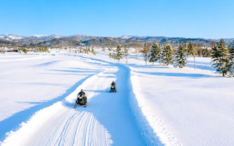 Snowmobiling on a snowy trail with trees and mountains in Bibai, Hokkaido.