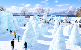 Winter festival with ice sculptures and visitors in Noboribetsu, Hokkaido, with Mt. Usu in the background.