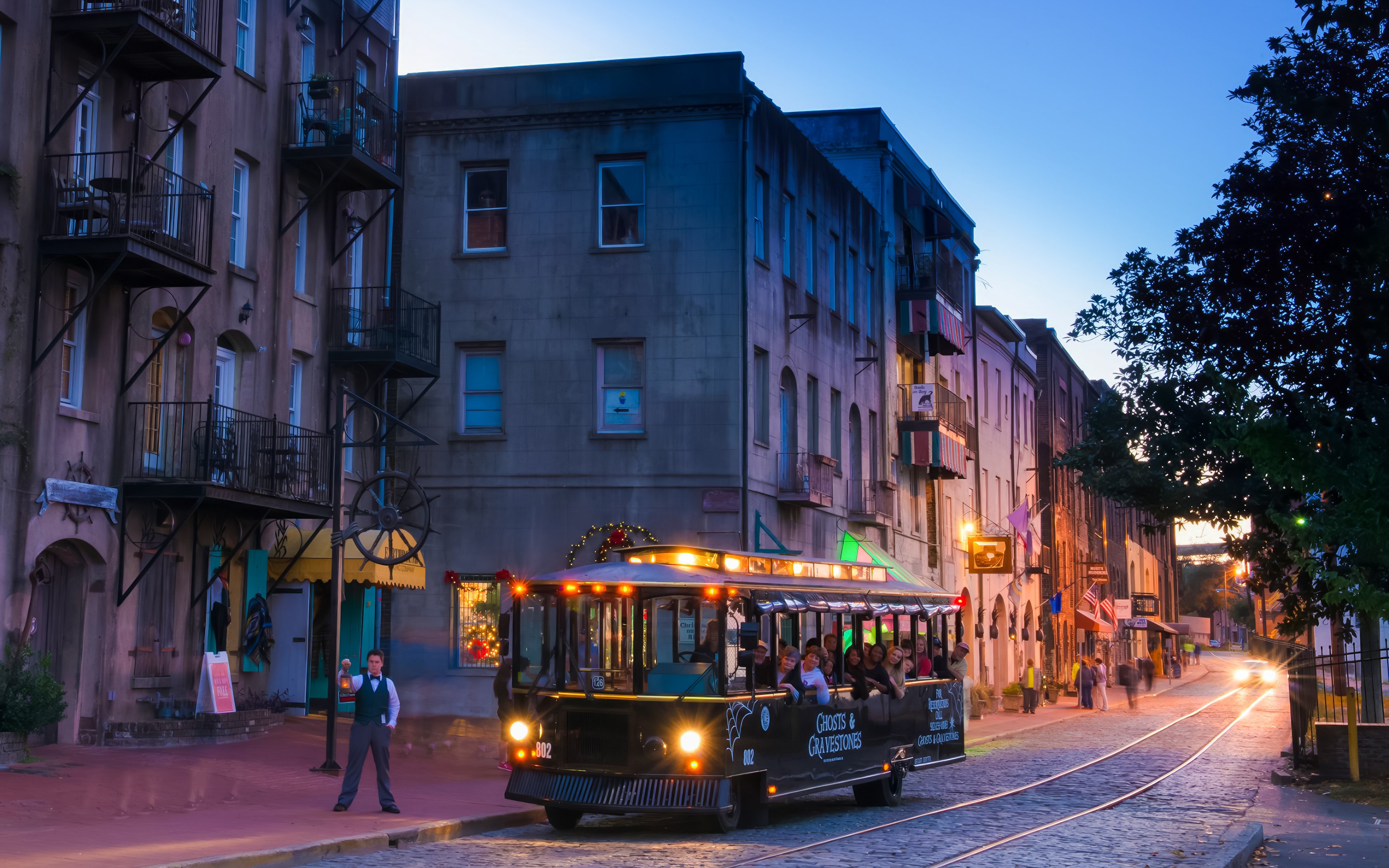 Ghosts & Gravestones tour trolley on a historic city street at dusk.