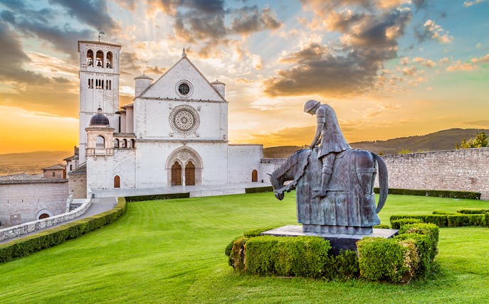 Basilica of Saint Francis of Assisi with equestrian statue at sunset, Assisi, Italy.