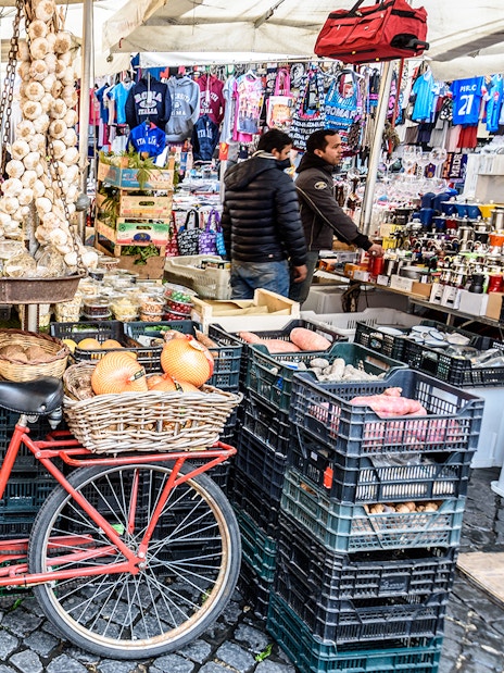 Red bicycle in front of fruit and vegetable stalls at Rome's Trionfale Market.