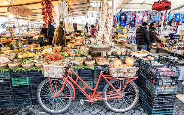 Red bicycle in front of fruit and vegetable stalls at Rome's Trionfale Market.