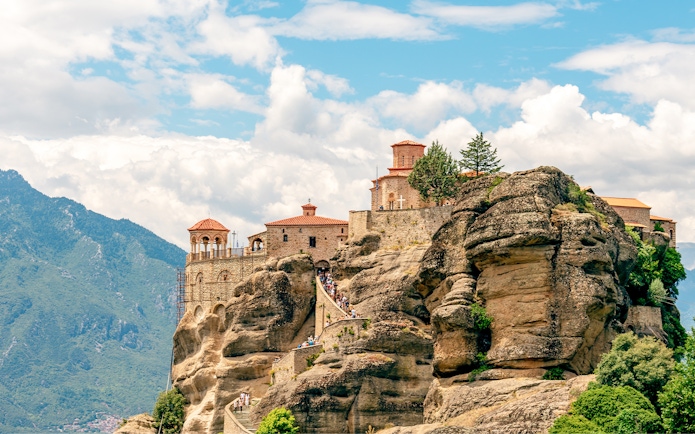 Monastery atop rock formations in Meteora, Greece, with visitors on a winding path.