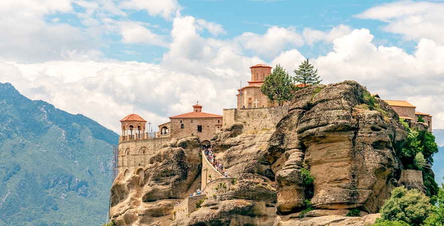 Monastery atop rock formations in Meteora, Greece, with visitors on a winding path.