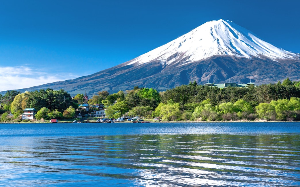 Mt. Fuji with snow-capped peak viewed from Lake Kawaguchiko, surrounded by lush greenery.