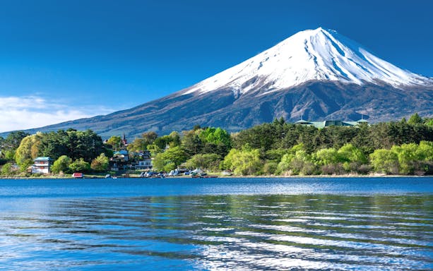 Mt. Fuji with snow-capped peak viewed from Lake Kawaguchiko, surrounded by lush greenery.