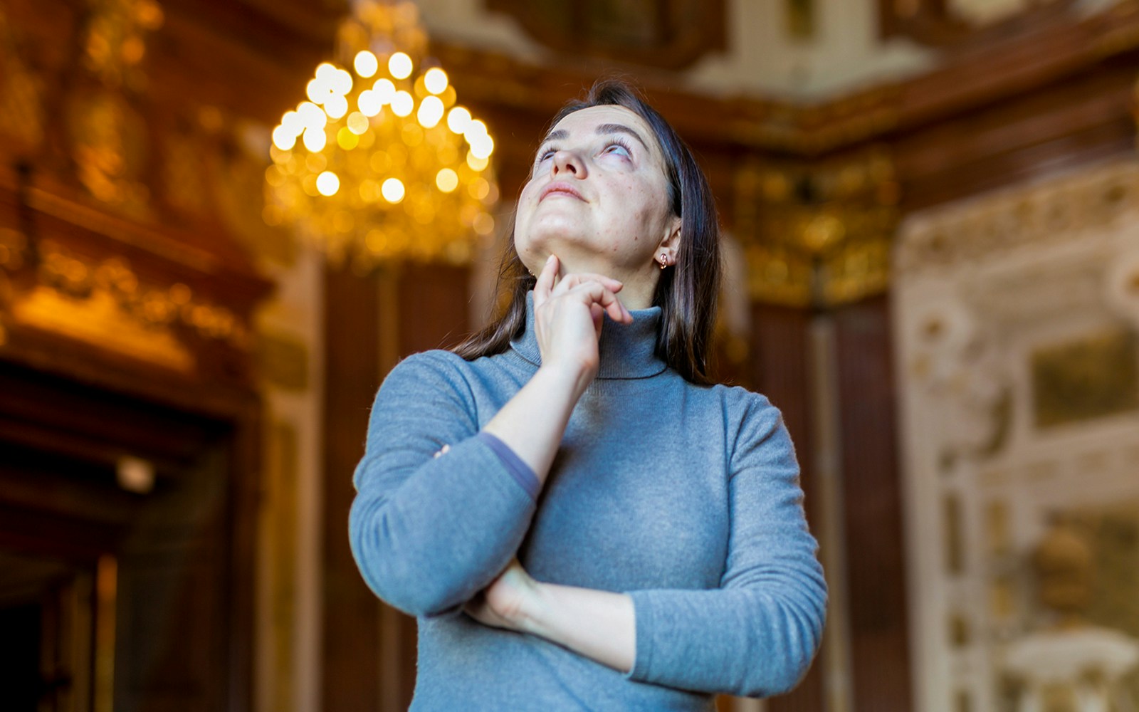 Museum visitor admiring ornate ceiling under chandelier.