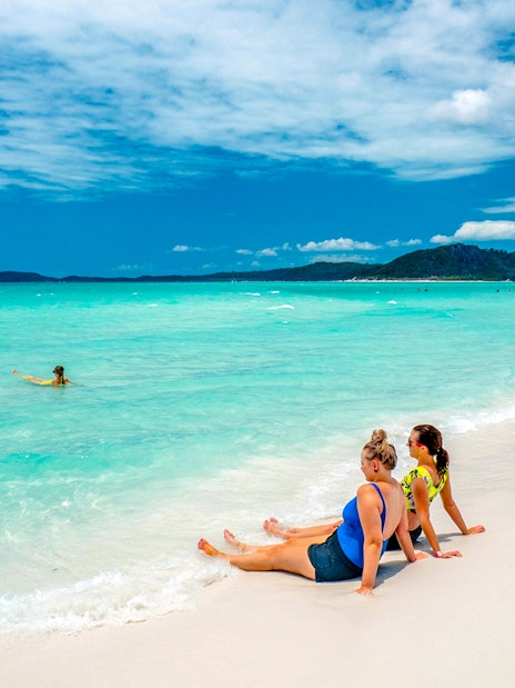 Tourists relaxing on Whitehaven Beach with turquoise water and distant hills.