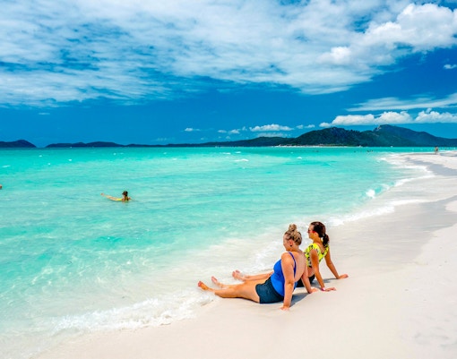 Tourists relaxing on Whitehaven Beach with turquoise water and distant hills.